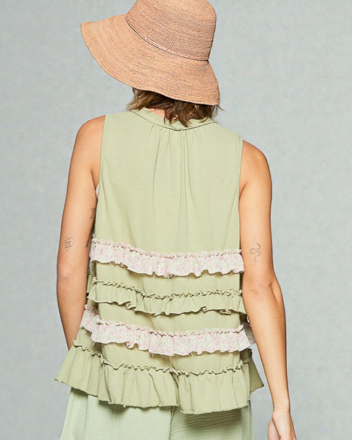 Person wearing a light green sleeveless top with ruffled layers and a straw hat on a gray background