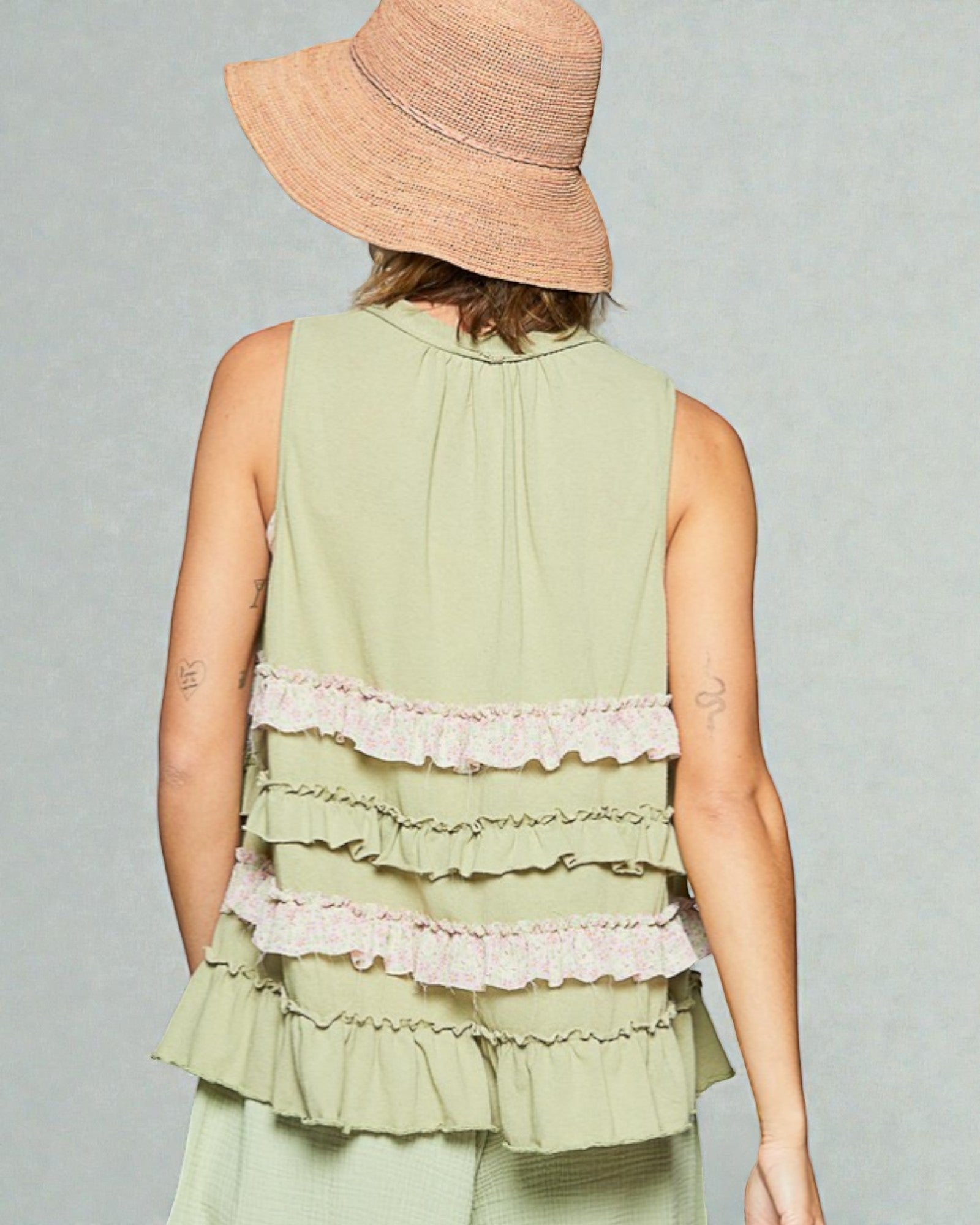 Person wearing a light green sleeveless top with ruffled layers and a straw hat on a gray background
