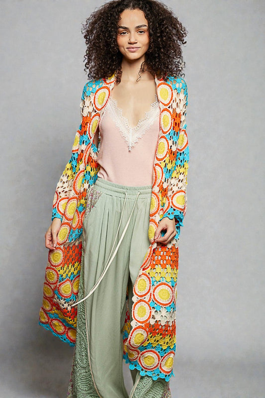 Woman wearing a colorful, patterned cardigan over a light pink top and green pants on a gray background