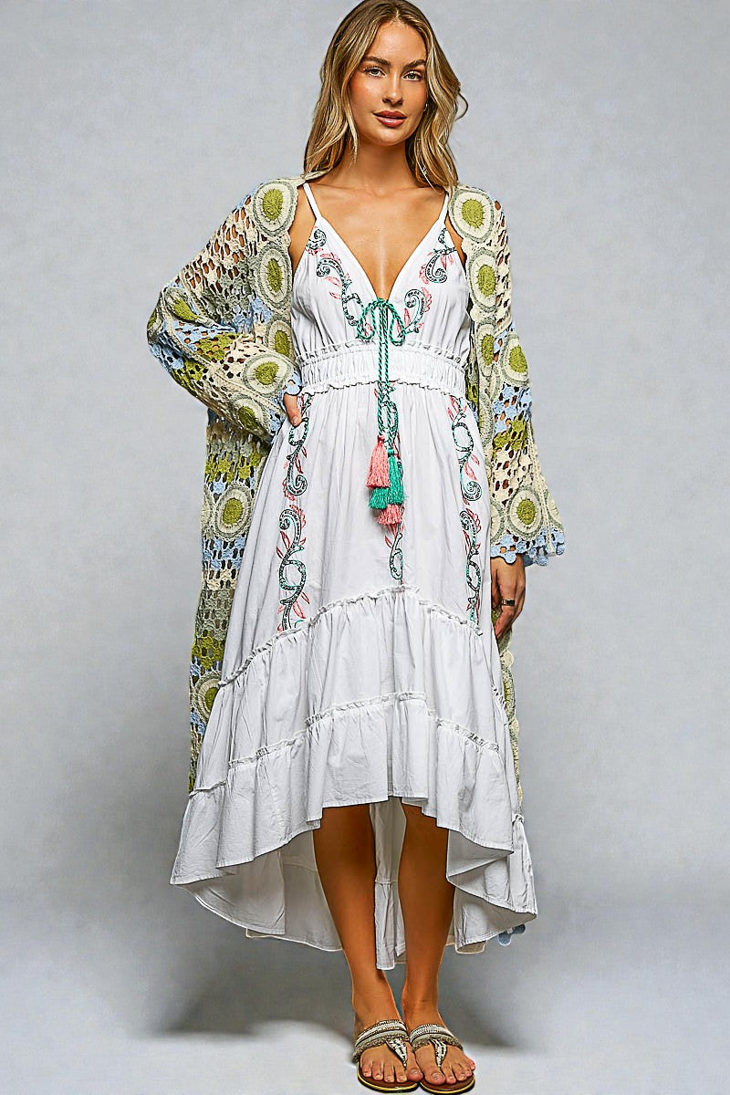 Woman wearing a white dress with floral patterns and a colorful kimono-style jacket on a gray background