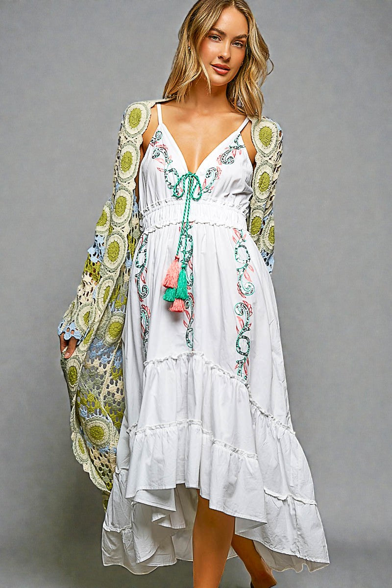 Woman wearing a white dress with floral embroidery and a colorful jacket on a gray background