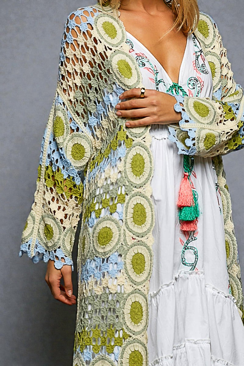 Woman wearing a colorful, patterned cardigan over a white dress with a gray background
