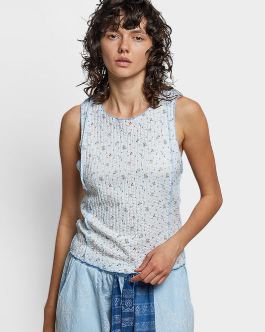 Woman wearing a light blue sleeveless top with a subtle pattern on a plain background