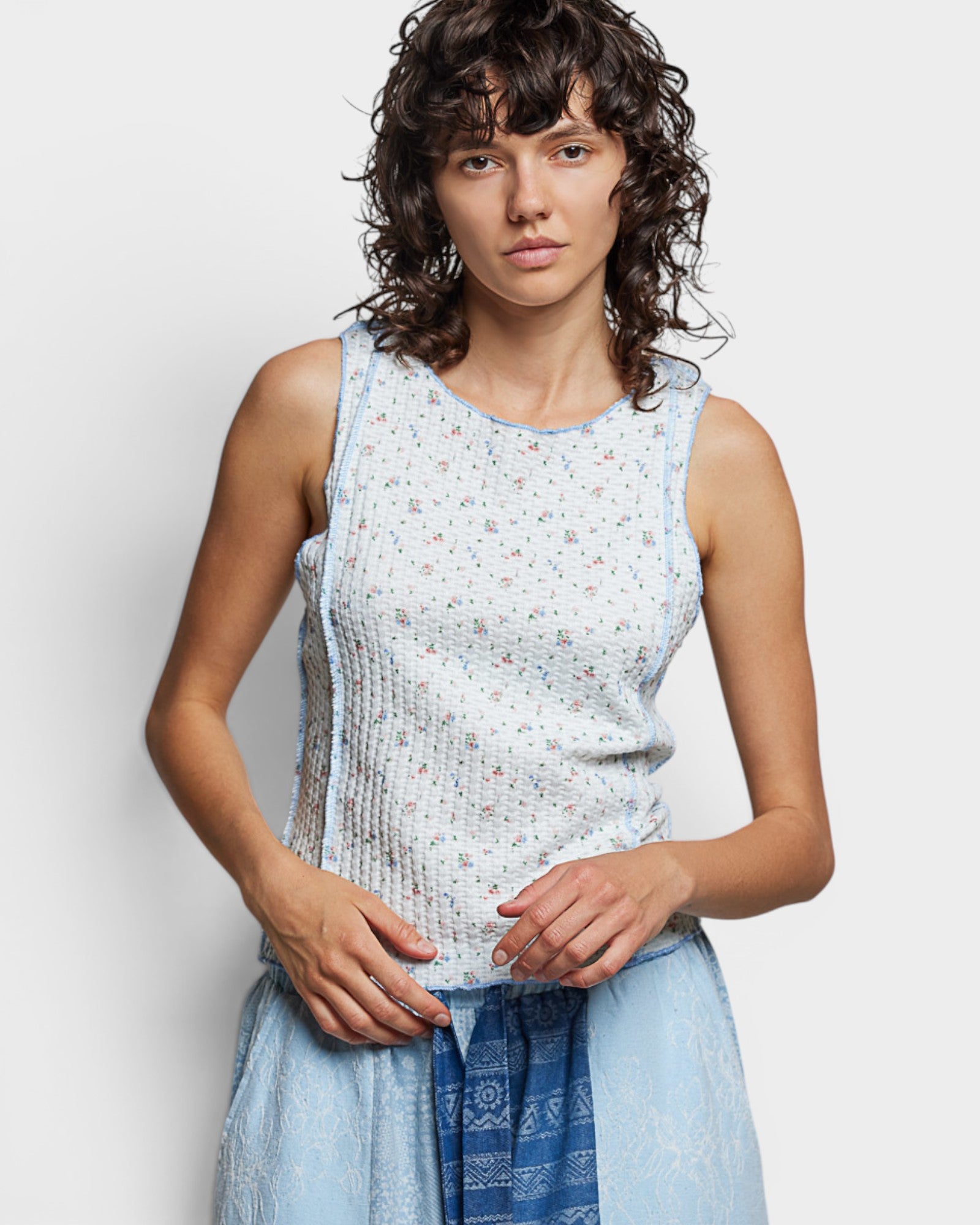 Woman wearing a light blue sleeveless top with a subtle pattern against a plain background
