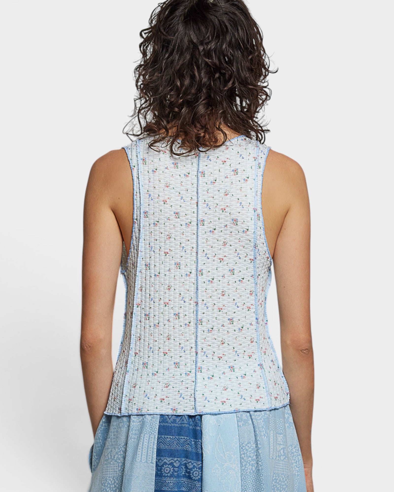Person wearing a light blue sleeveless top with a subtle pattern on a white background
