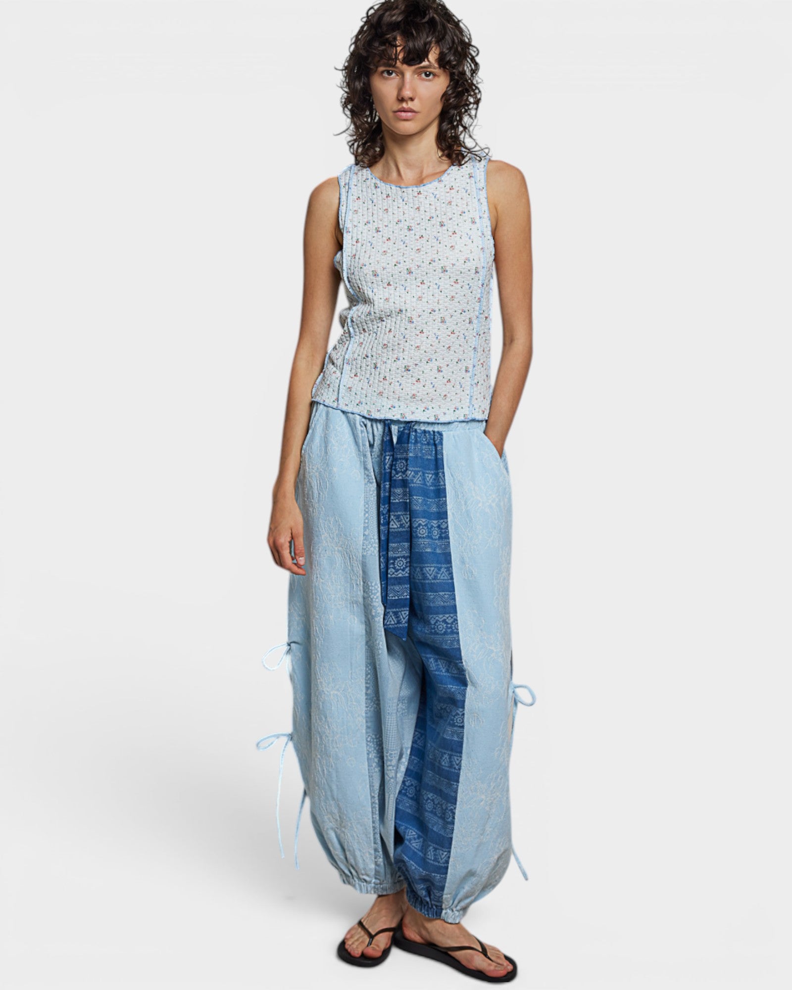 Woman wearing a sleeveless top and long light blue pants on a white background