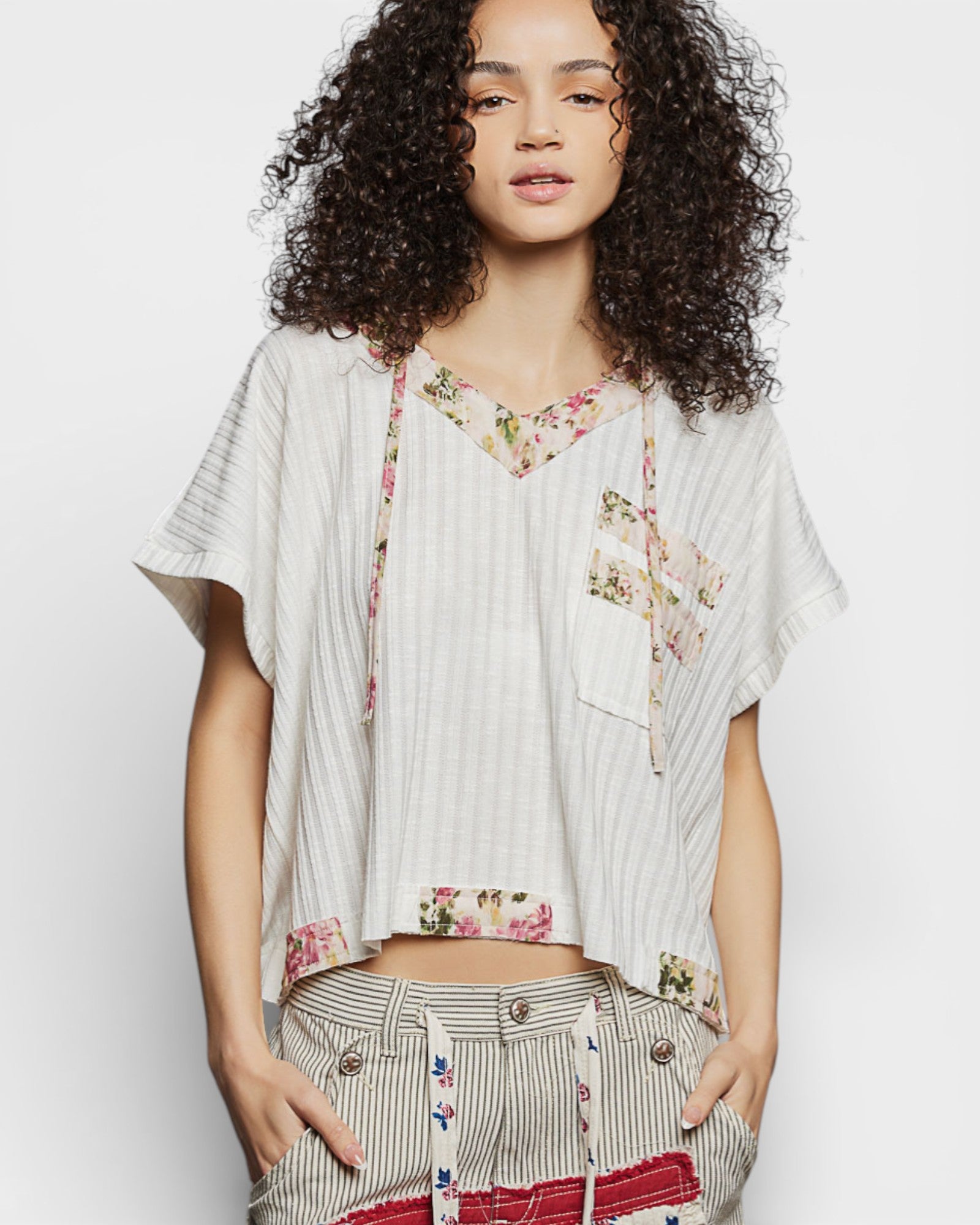 Woman wearing a white blouse with floral patterns and striped pants on a plain background