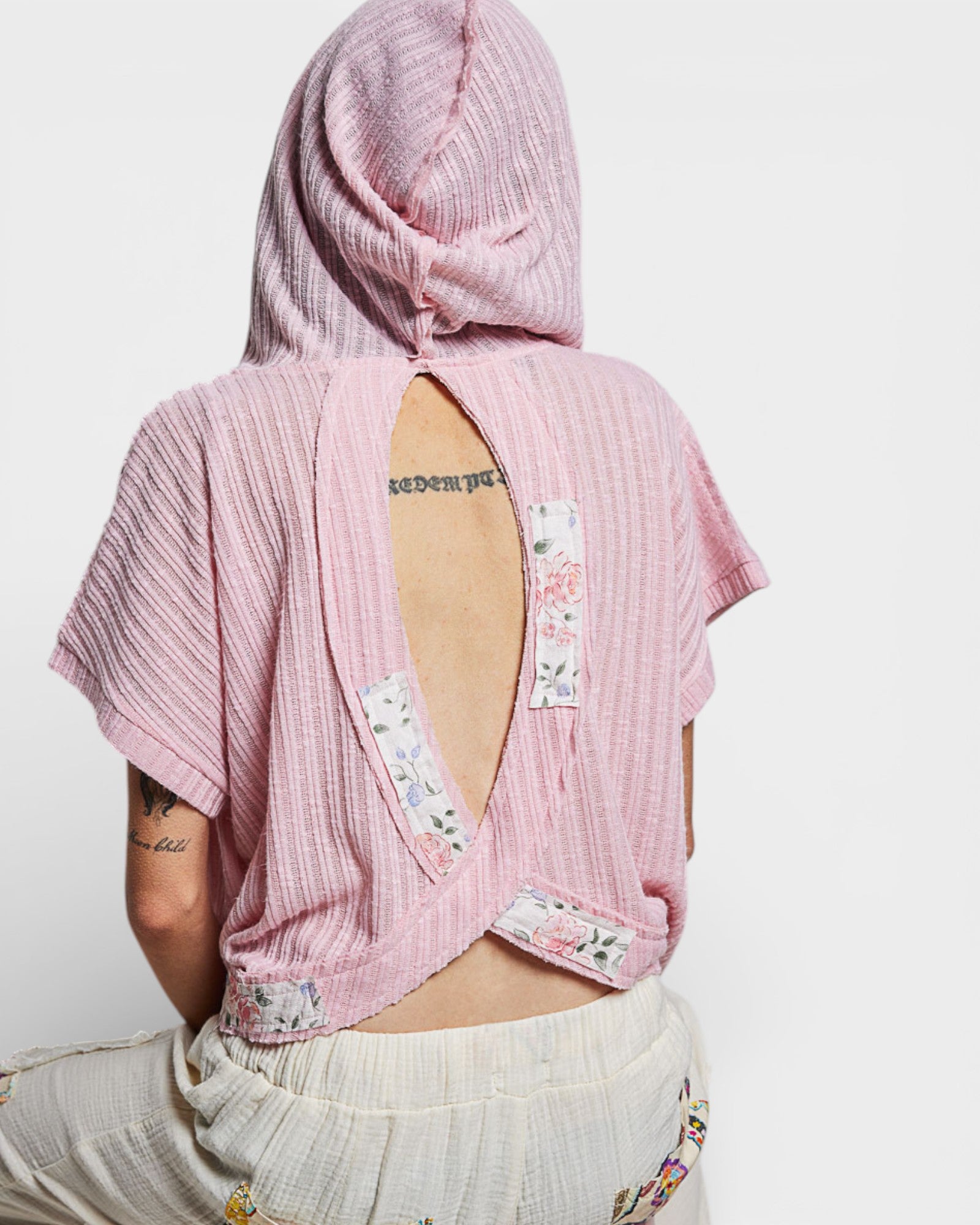 Person wearing a pink textured top with floral patches on a white background