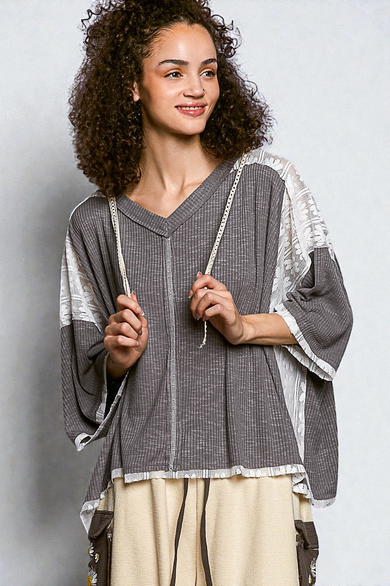 Woman wearing a gray and white patterned top with beige pants against a plain background