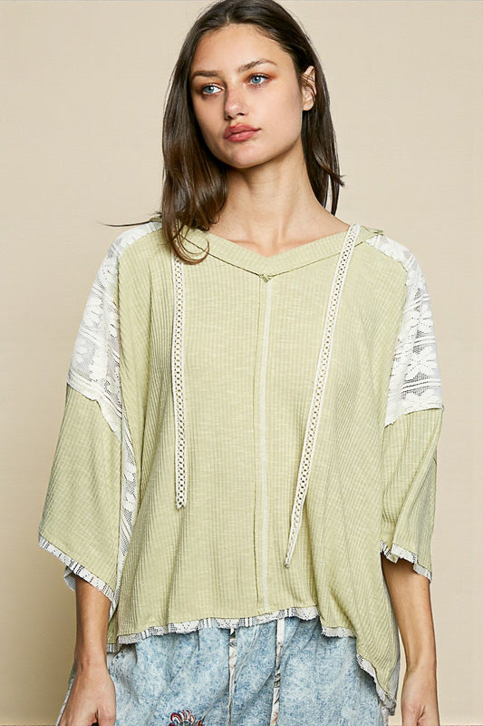 Woman wearing a light green top with white lace details on a beige background