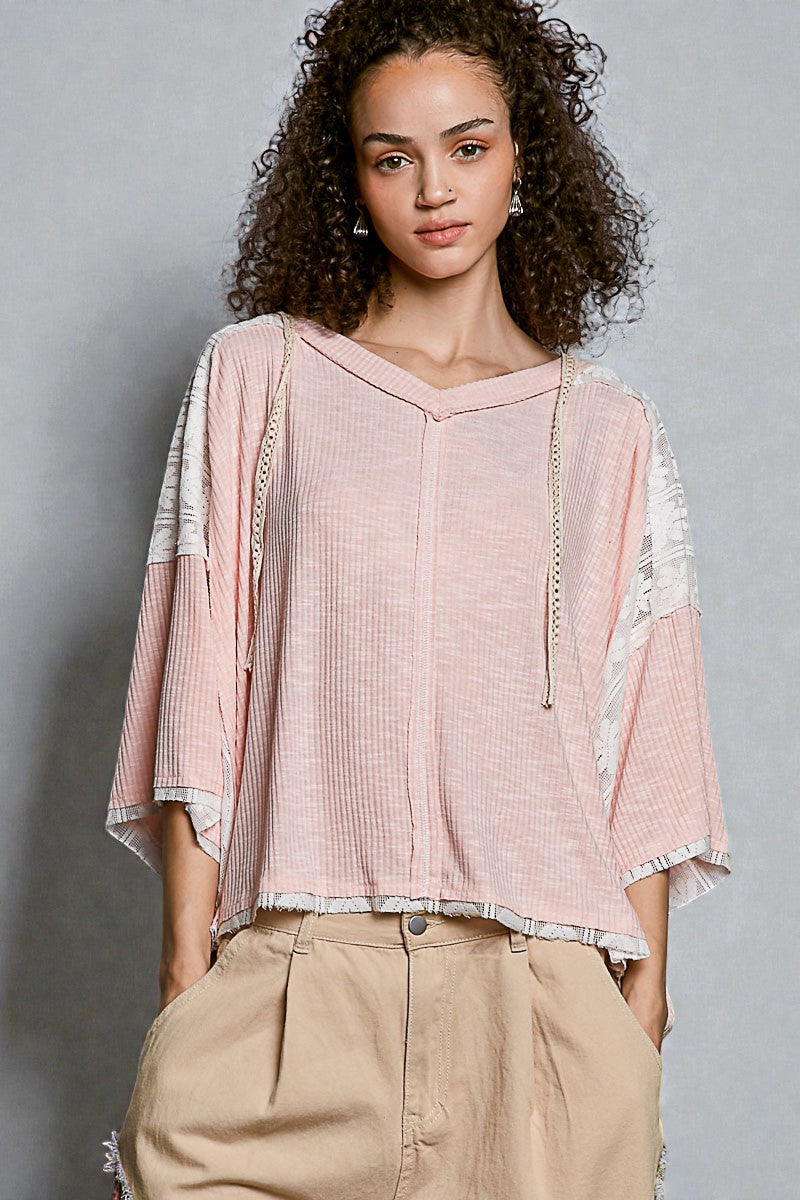 Woman wearing a pink blouse with lace sleeves against a gray background