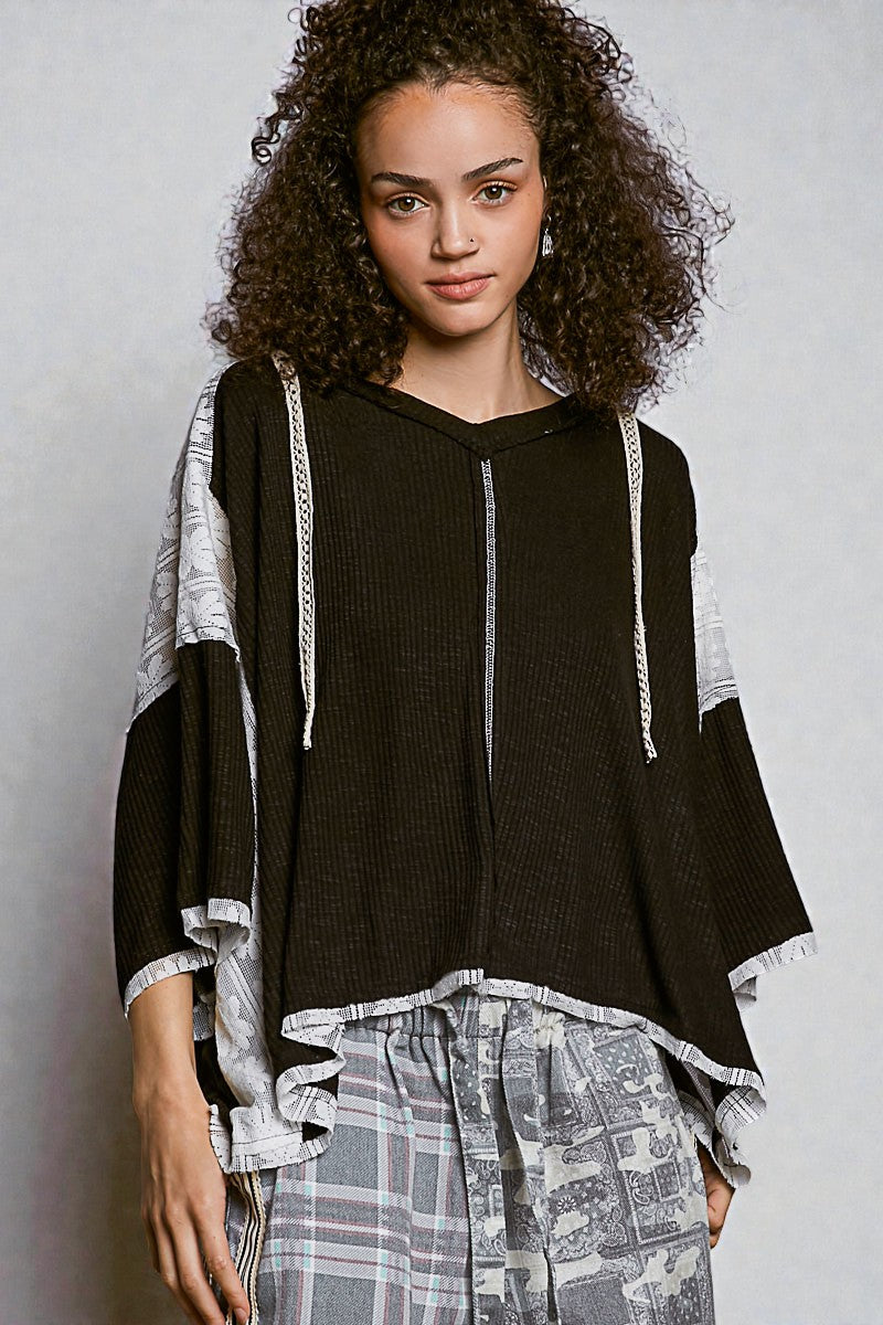 Woman wearing a black hoodie with white accents and plaid pants on a gray background