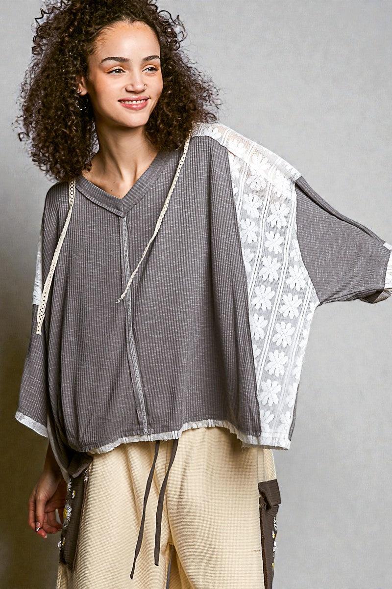 Woman wearing a gray and white patterned top with beige pants against a gray background