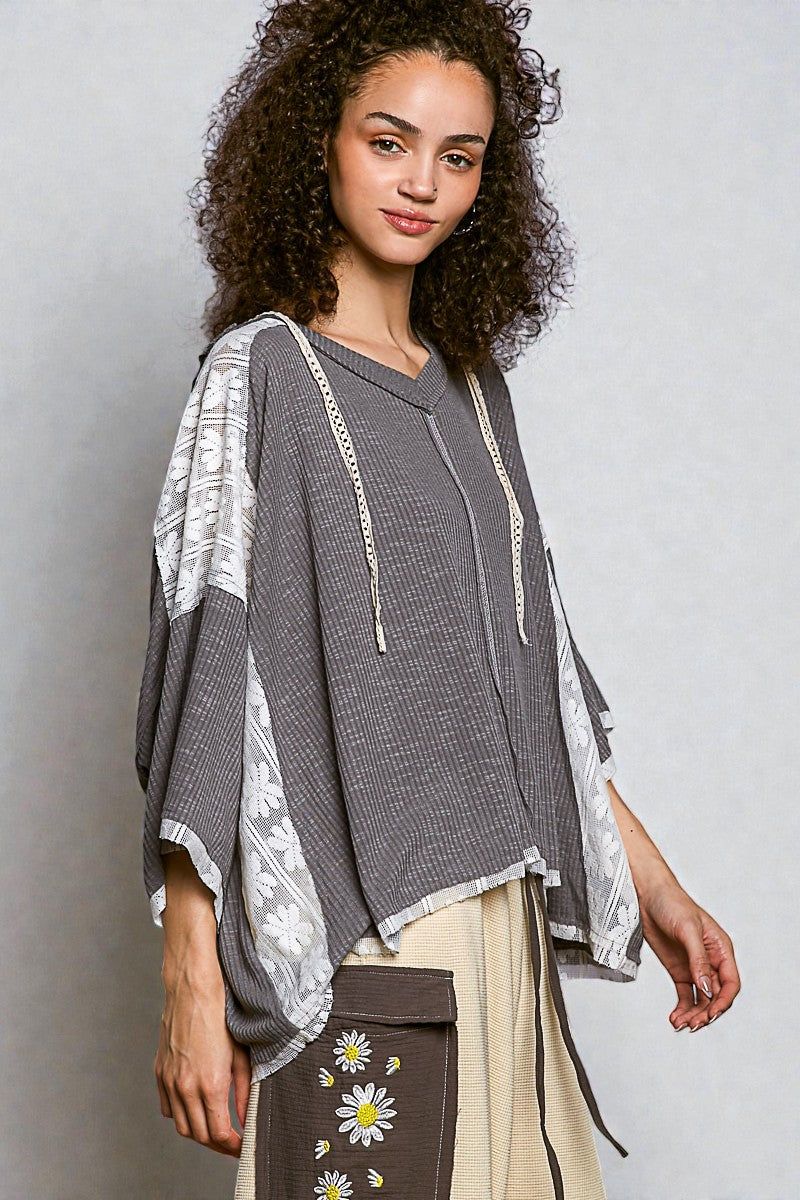 Woman wearing a gray top with white lace details on a plain background