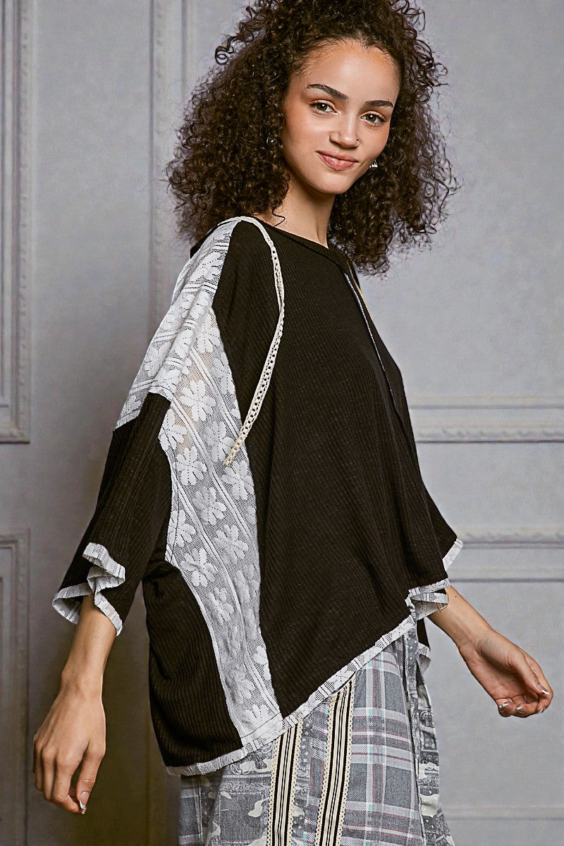 Woman wearing a black top with a patterned kimono-style jacket against a gray wall.