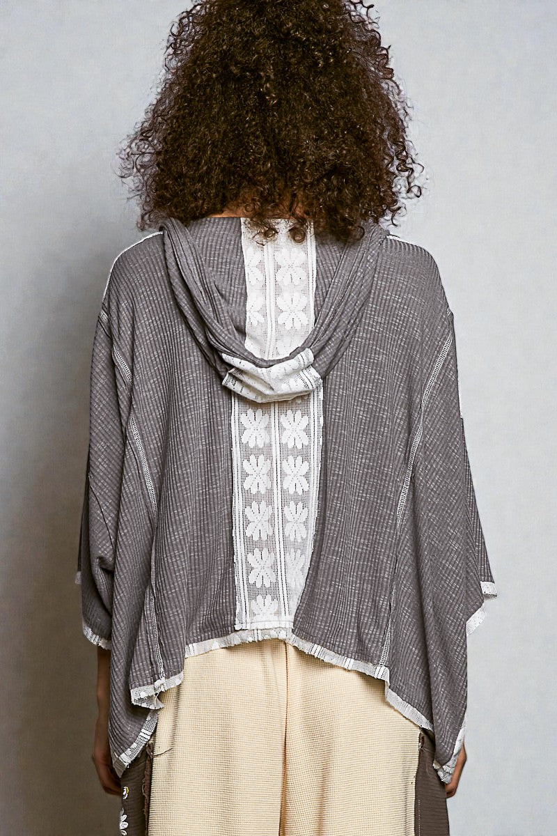Person wearing a gray checkered shawl over a white lace top and beige pants on a plain background