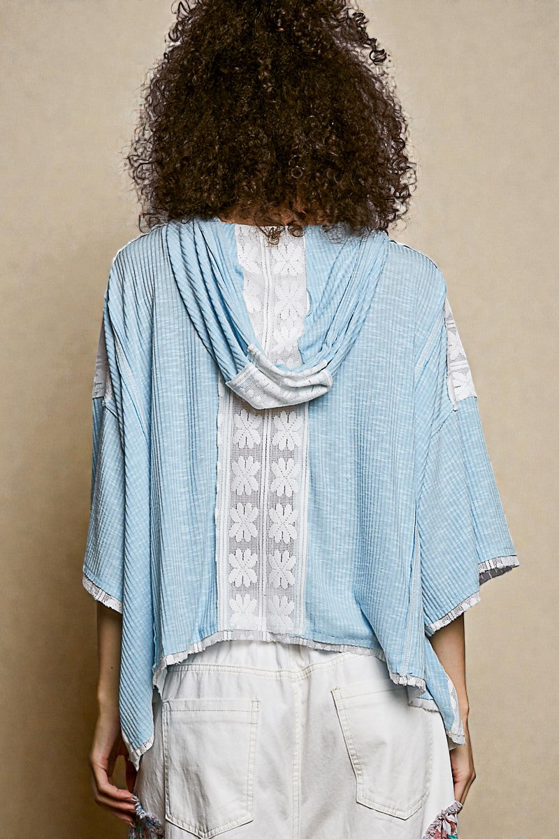 Person wearing a light blue kimono-style garment over a white lace top on a beige background