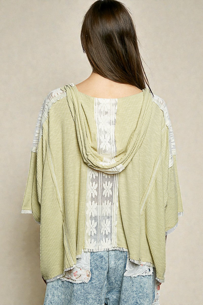 Woman wearing a light green cardigan with lace details over a white top and blue jeans on a beige background