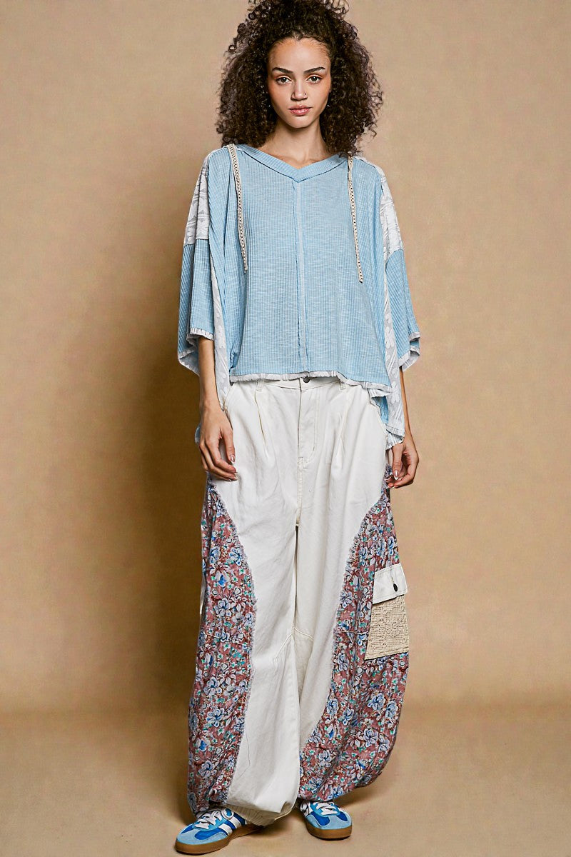 Woman wearing a blue top and white pants with floral patterns against a beige background