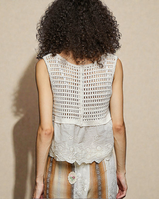 Person wearing a sleeveless crochet top with a neutral background