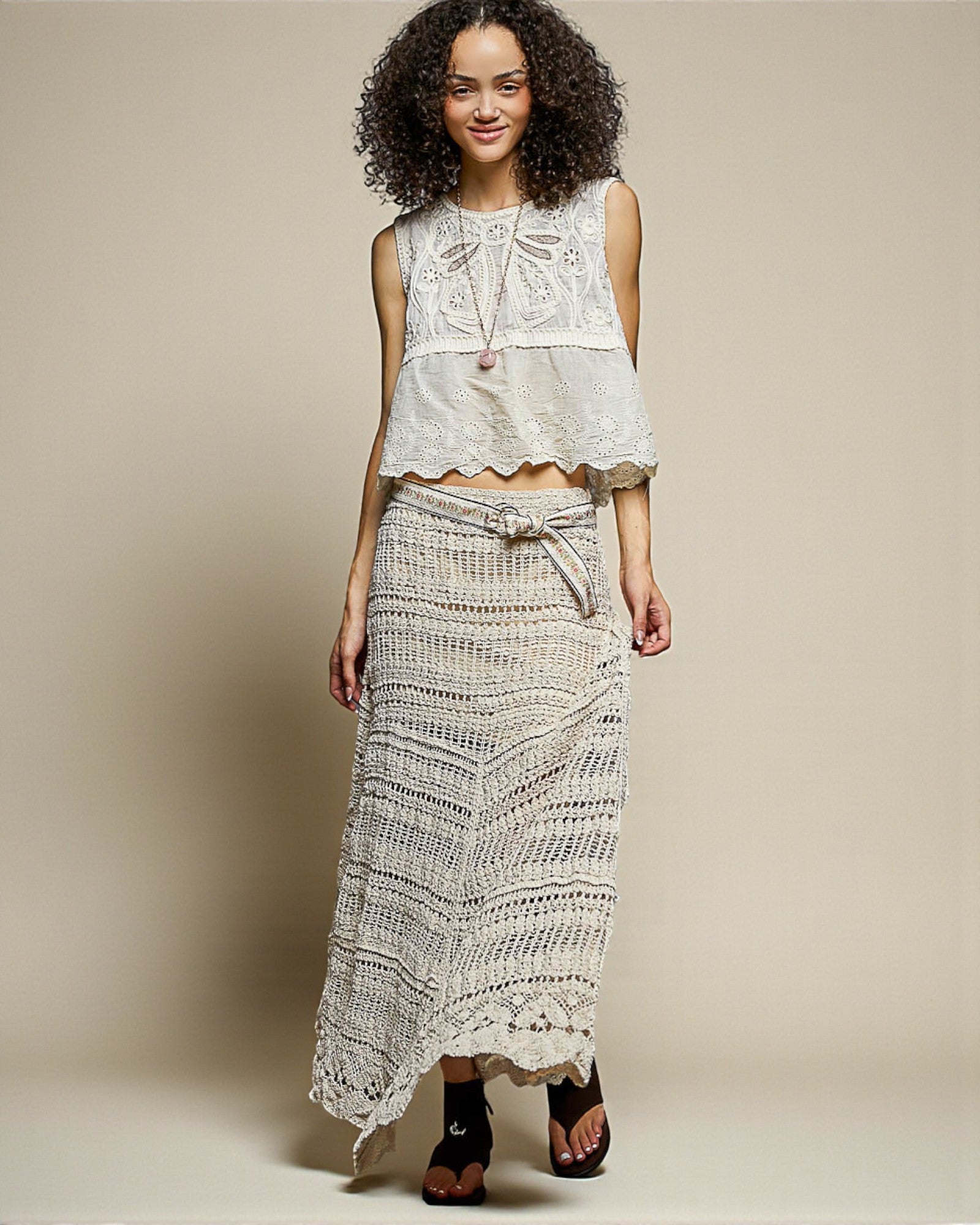 Woman wearing a white lace top and long skirt against a beige background