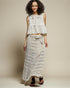 Woman wearing a white lace top and long skirt against a beige background