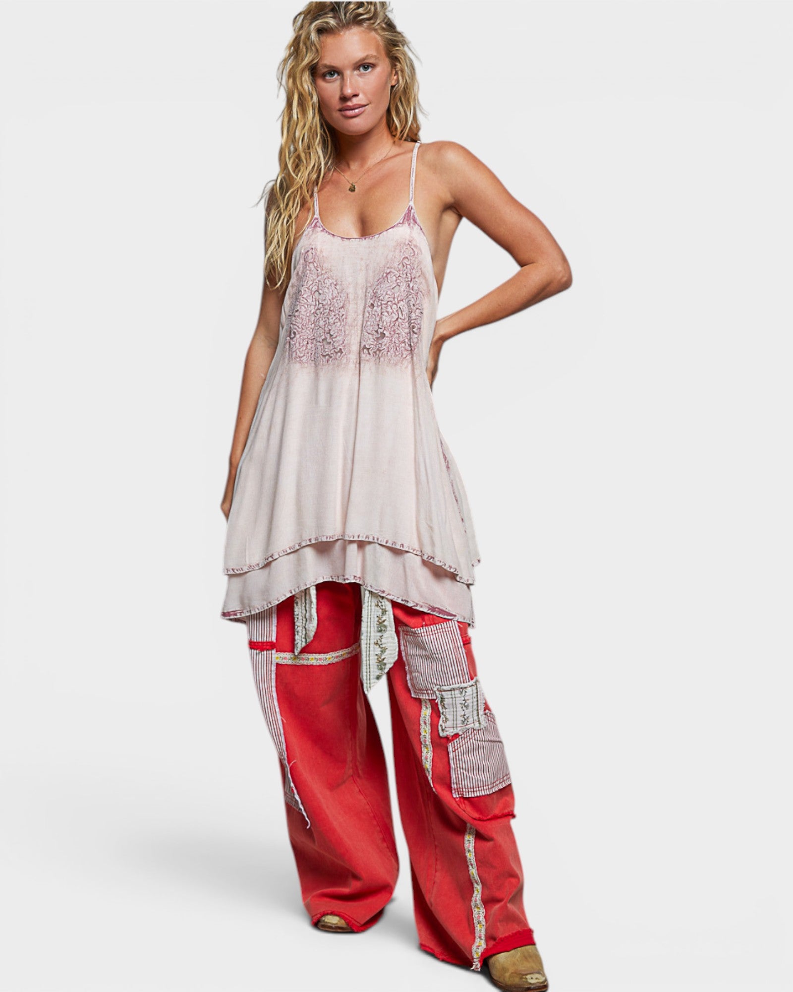 Woman wearing a layered outfit with a white top and red pants on a plain background