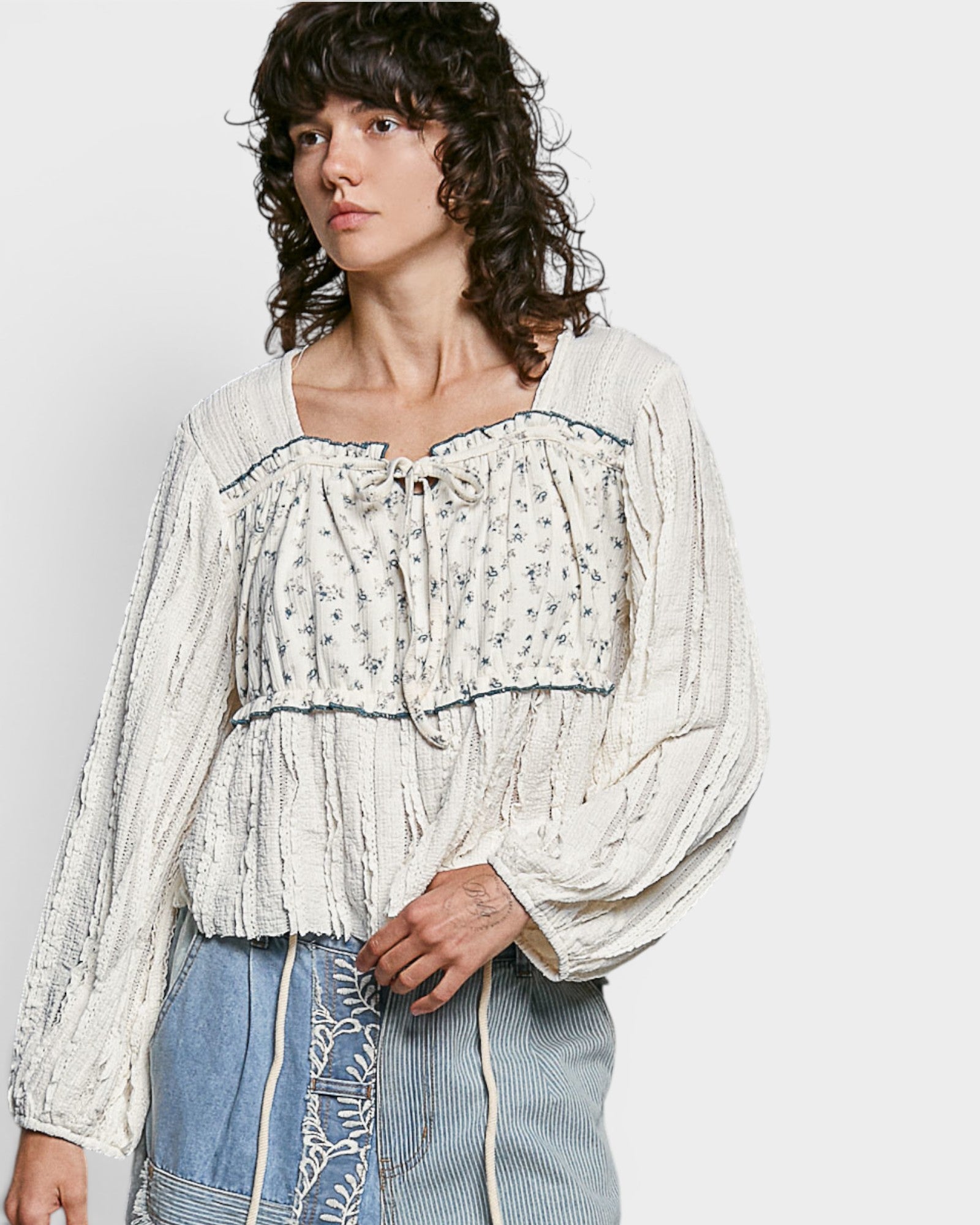 Woman wearing a white blouse with lace details against a plain background