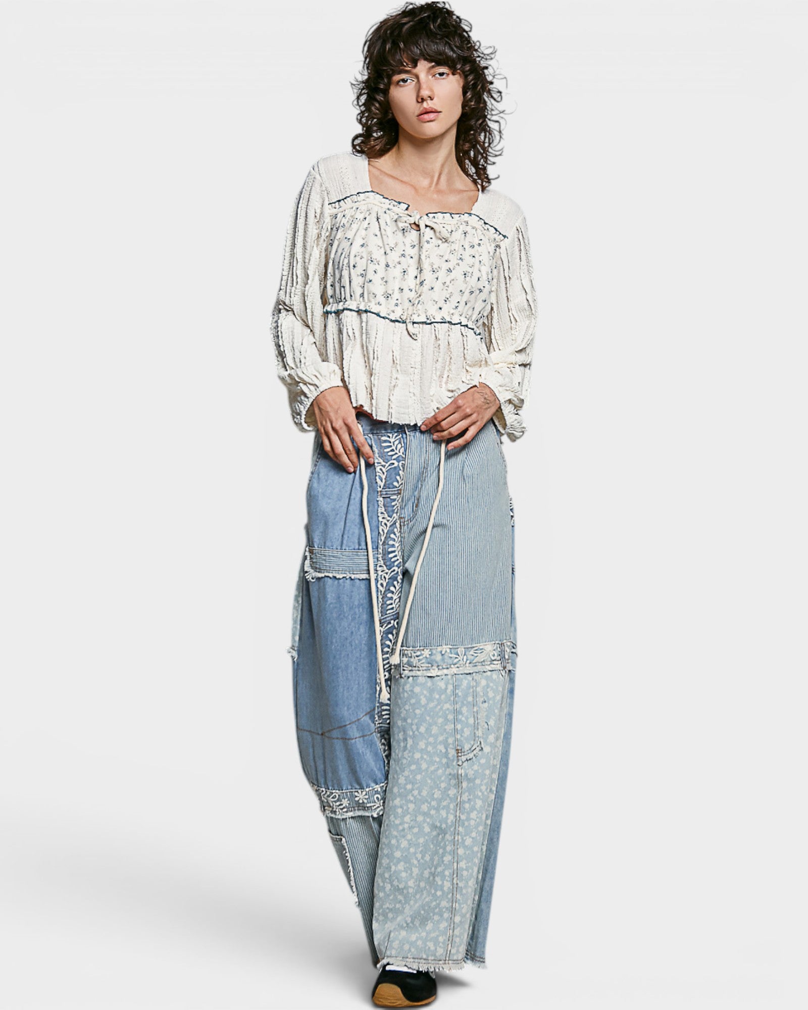 Woman wearing a white blouse and blue denim pants with lace details on a white background