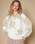 Woman wearing a white blouse with floral embroidery against a beige background