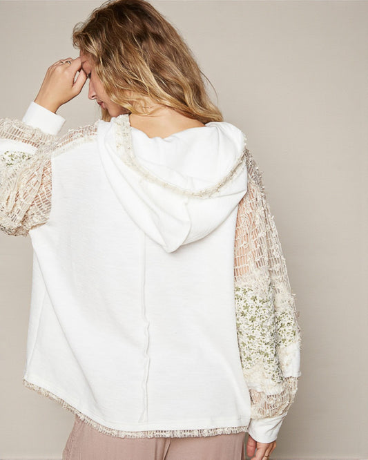 Woman wearing a white hoodie with sheer sleeves against a neutral background