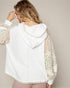 Woman wearing a white hoodie with sheer sleeves against a neutral background