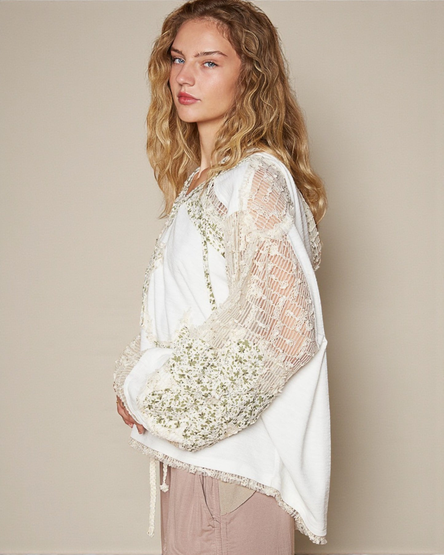Woman wearing a white lace top holding flowers against a beige background