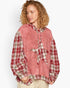 A woman wearing a unique patchwork hoodie with a dusty pink textured front panel and red, green, and white plaid sleeves and hood, paired with beige pants against a light gray background.