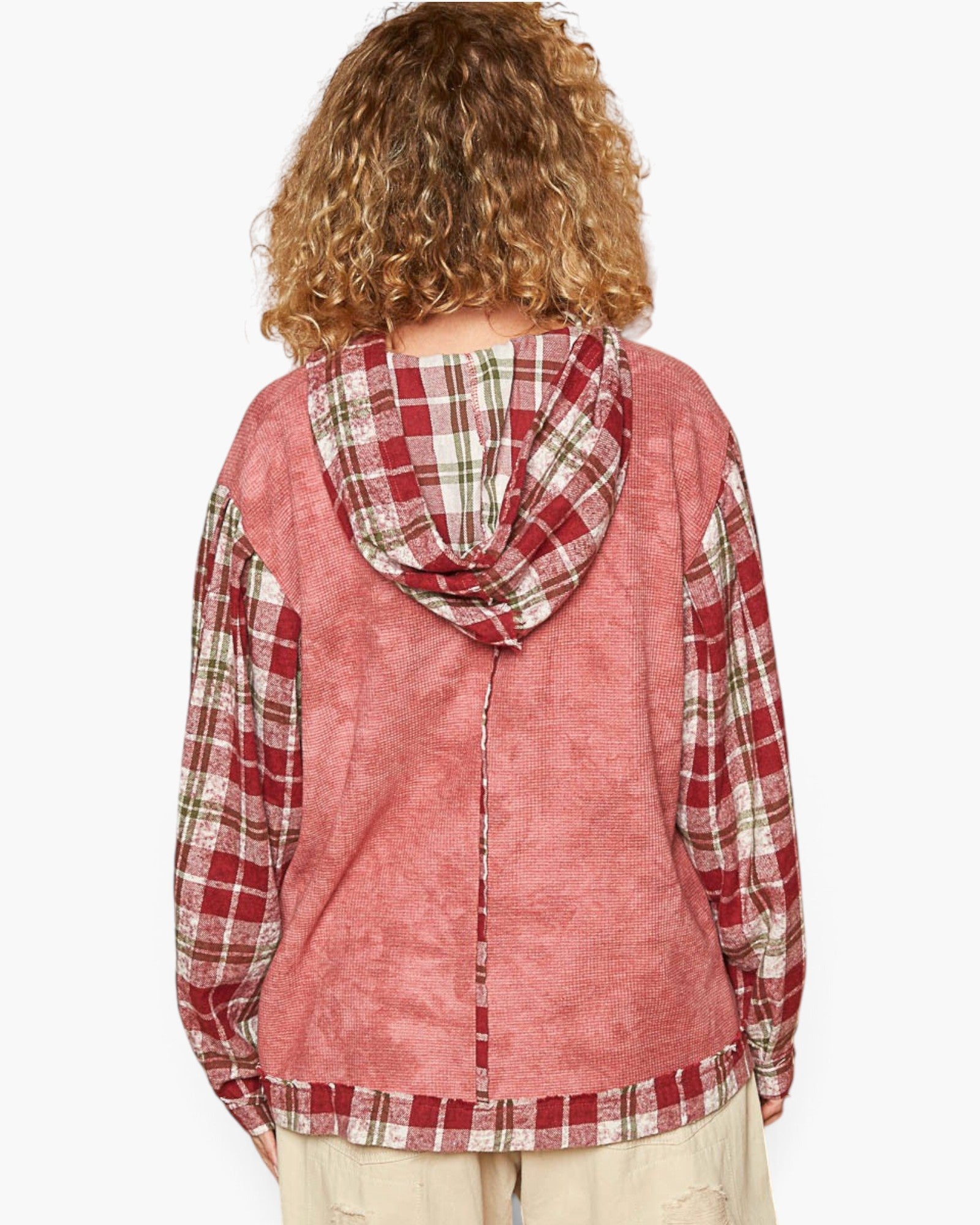 A person shown from the back wearing a hooded jacket with a dusty rose body and red, green, and white plaid hood and sleeves, paired with light beige pants against a plain white background.