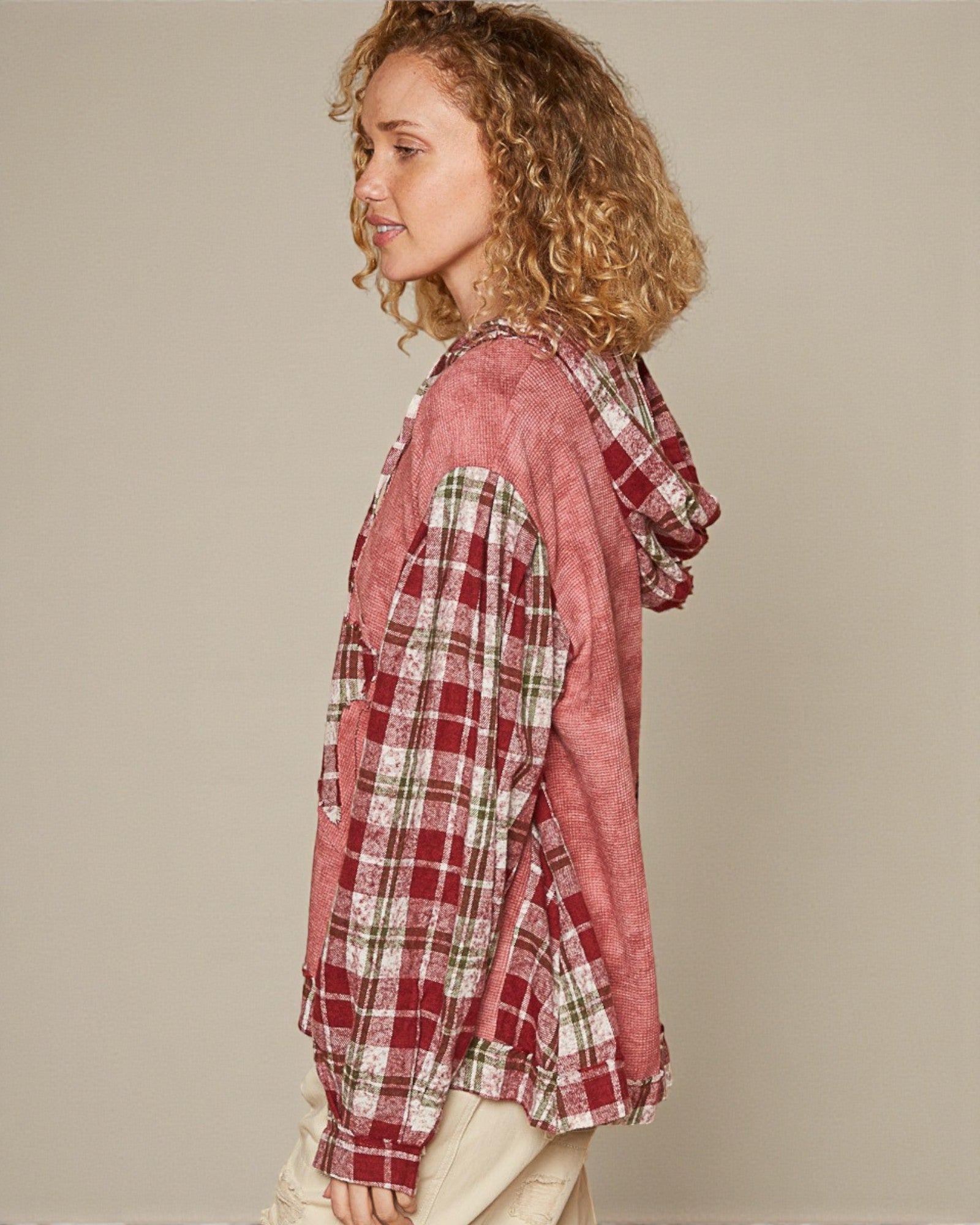 Woman wearing a red plaid shirt over a pink hoodie against a beige background
