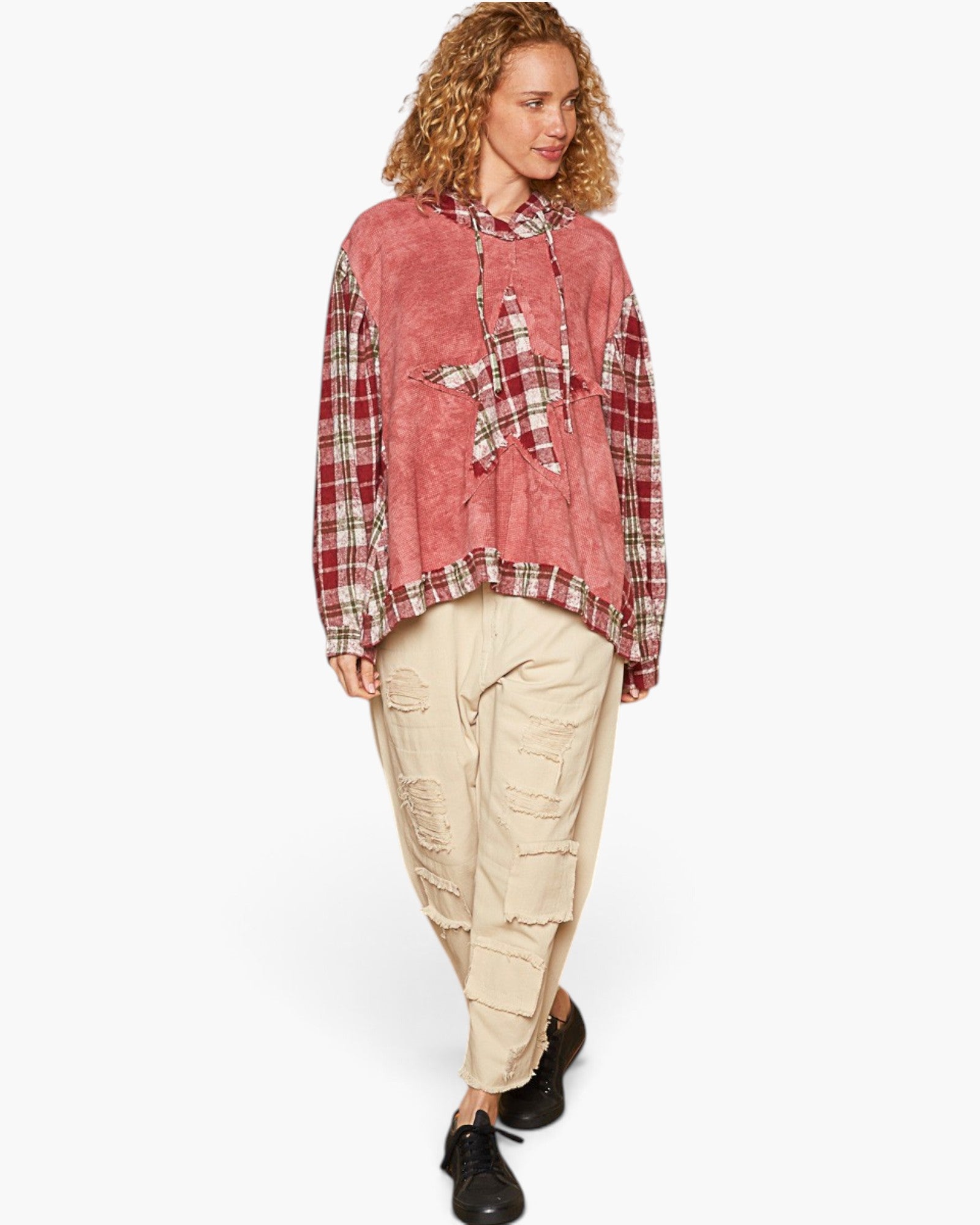 A model wearing a dusty pink and red plaid patchwork hoodie with a star patch, paired with beige distressed cargo pants and black shoes, against a plain white background.