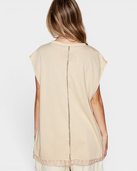 Woman wearing a beige sleeveless top with sheer overlay on a white background