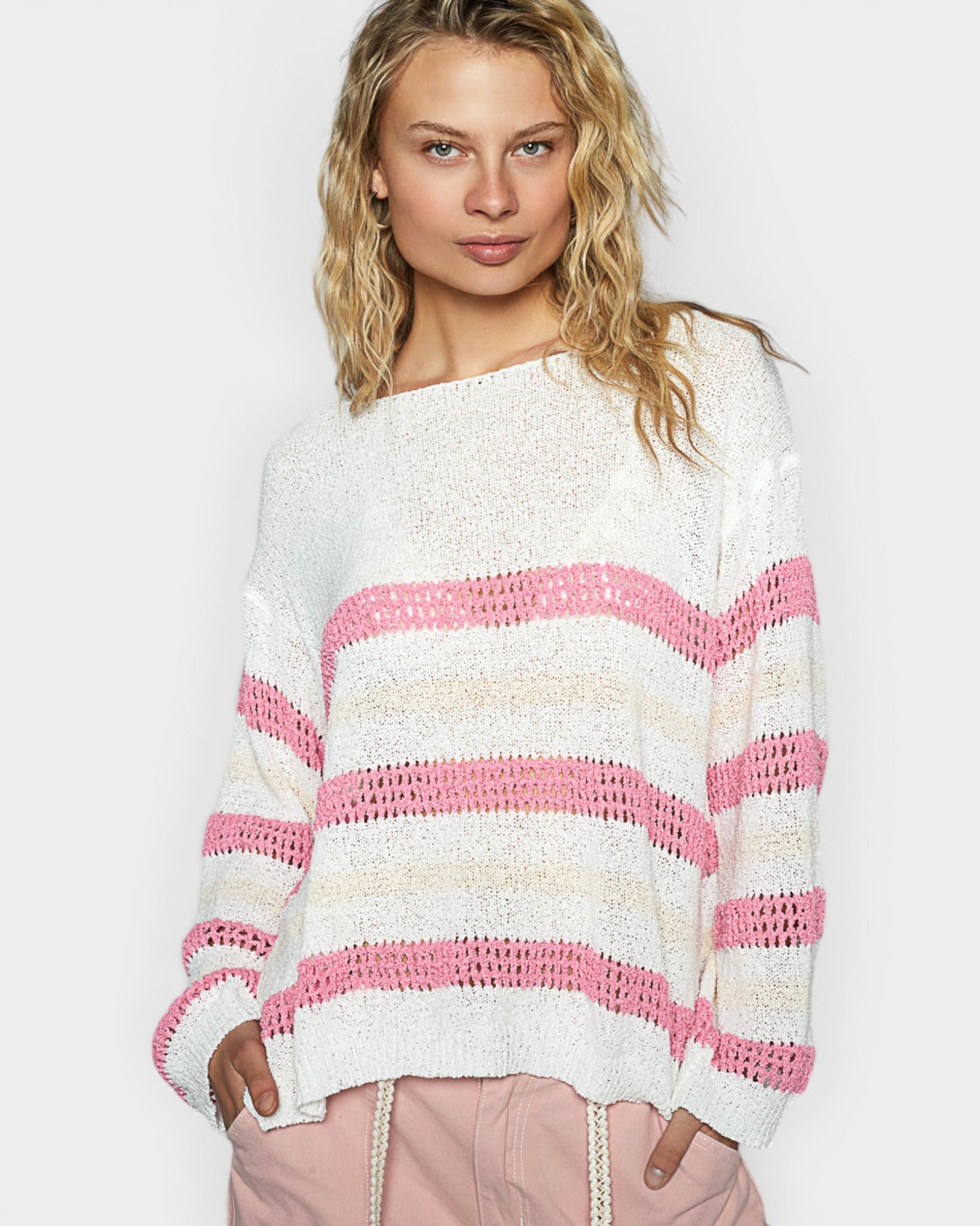 Woman wearing a white sweater with pink and beige stripes on a plain background