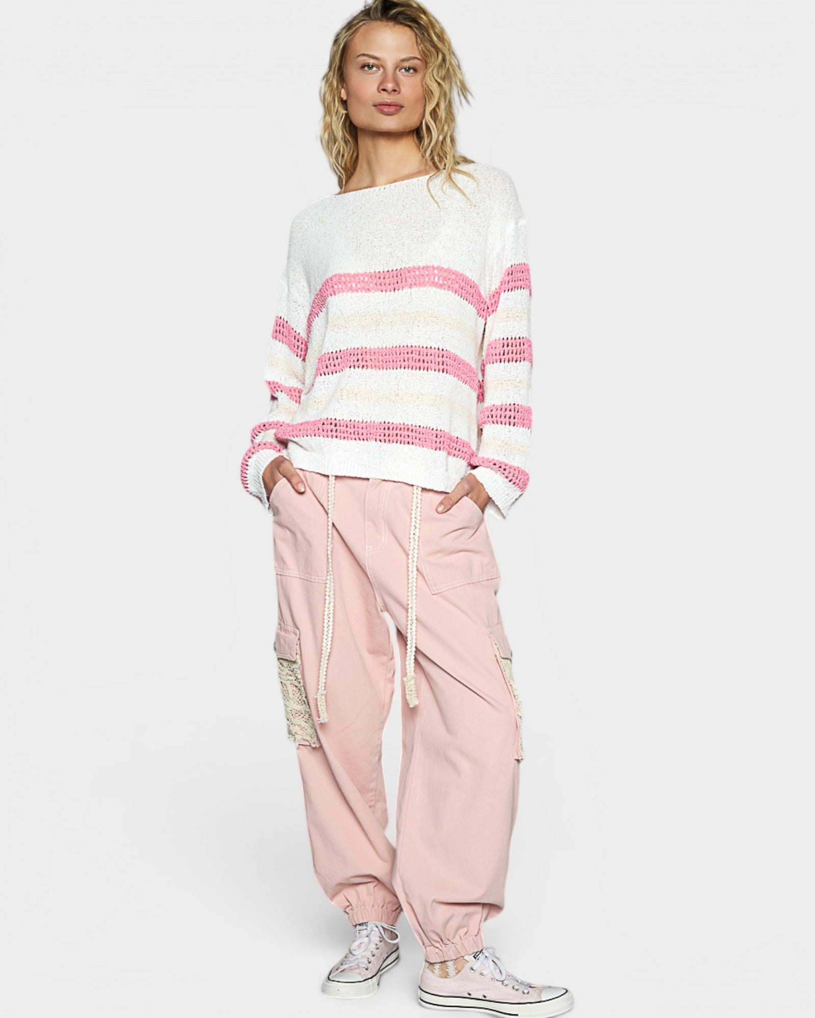Person wearing a white and pink striped sweater with pink pants on a light gray background