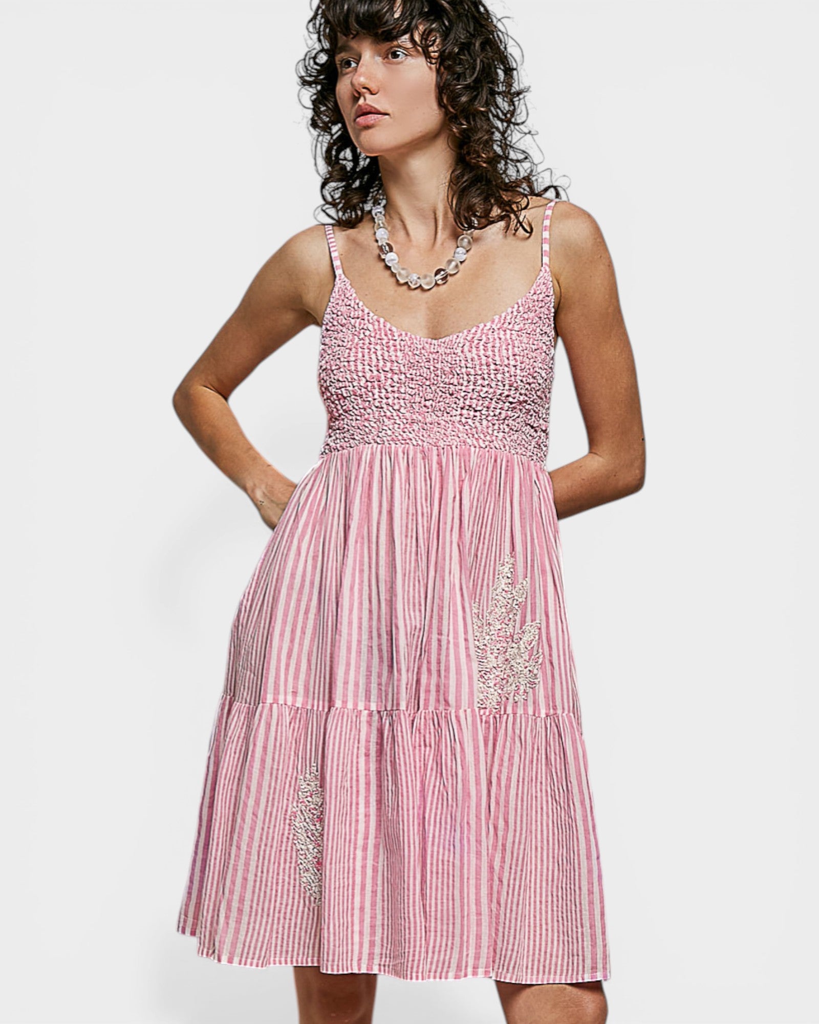 Woman wearing a pink dress with white stripes and embellishments on a white background