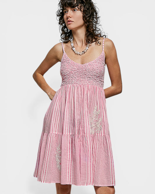 Woman wearing a pink dress with white stripes and embellishments on a white background