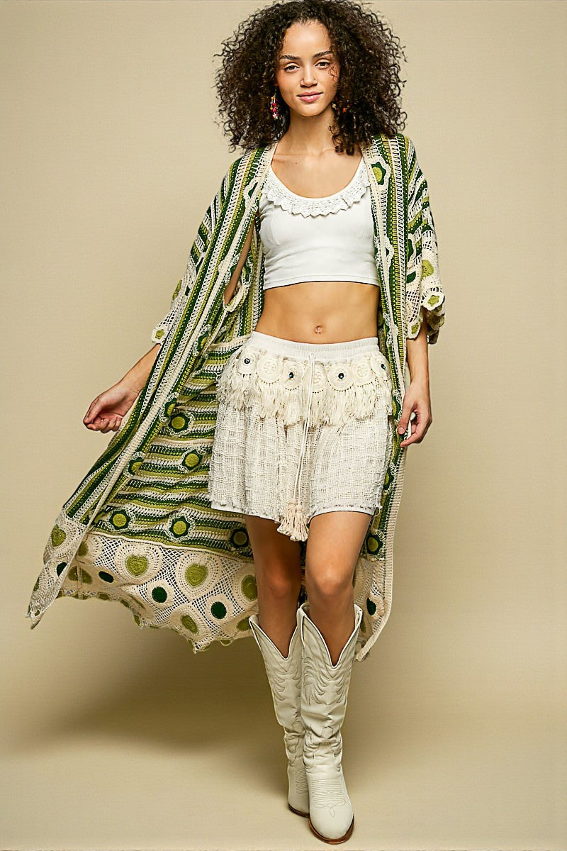 Woman wearing a long green and white patterned kimono over a white outfit with a beige background