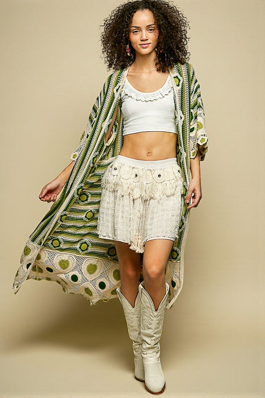Woman wearing a long green and white patterned kimono over a white outfit with a beige background