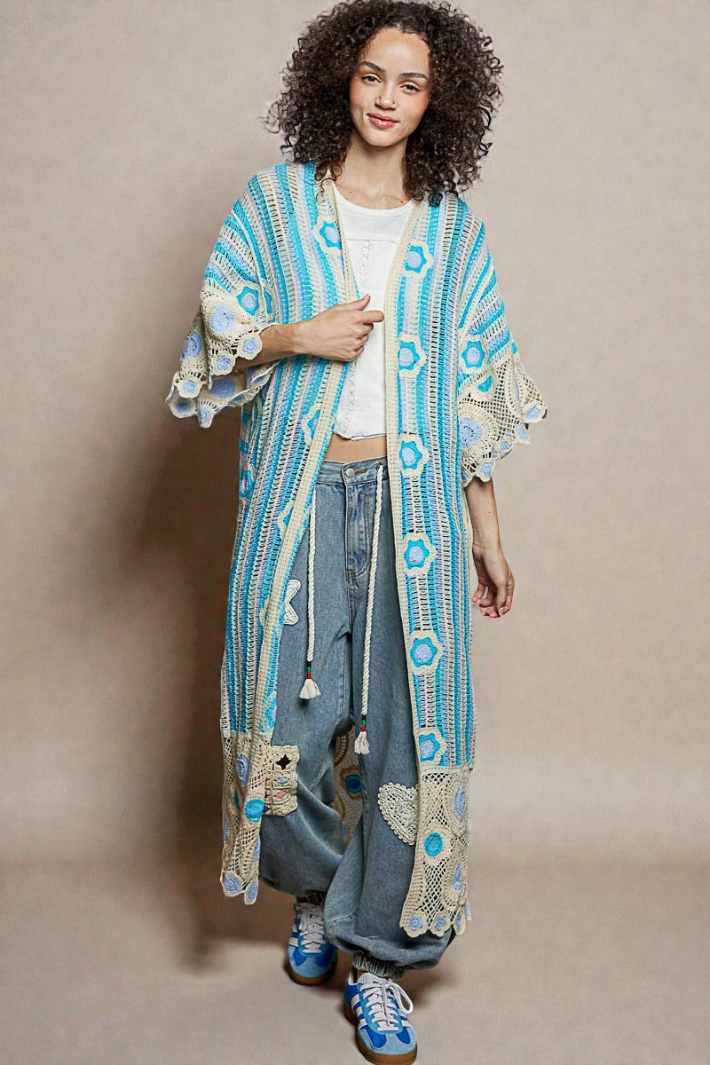 Woman wearing a blue and white patterned kimono-style jacket with wide-leg jeans on a beige background