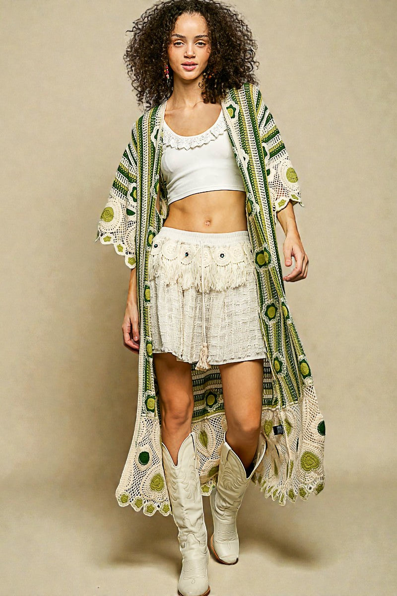 Woman wearing a long, patterned kimono over a white outfit with white boots on a beige background