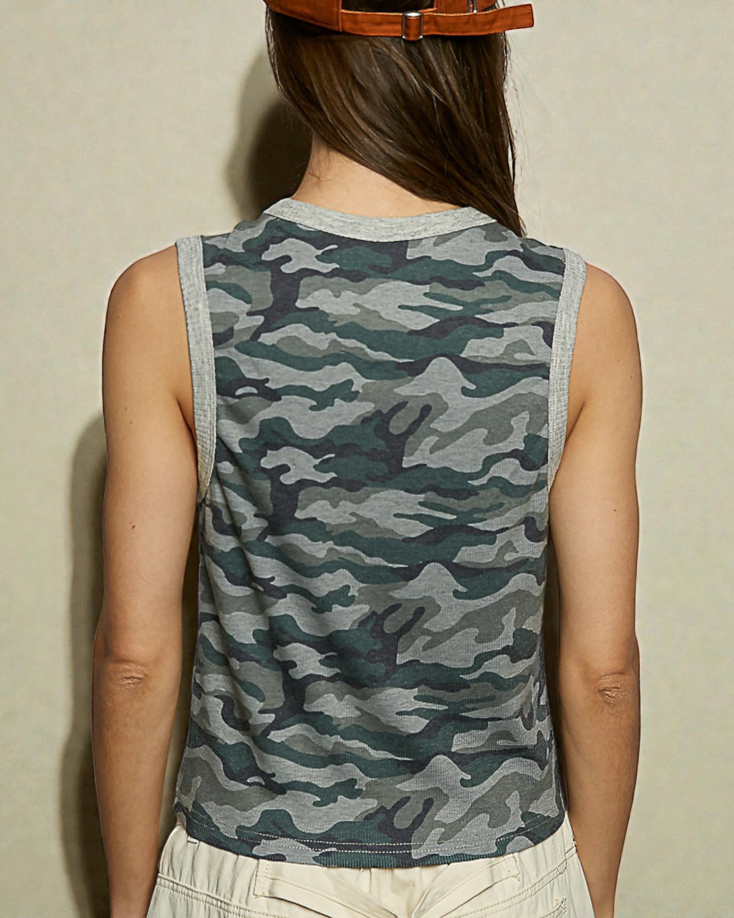 Person wearing a camouflage sleeveless shirt against a neutral background