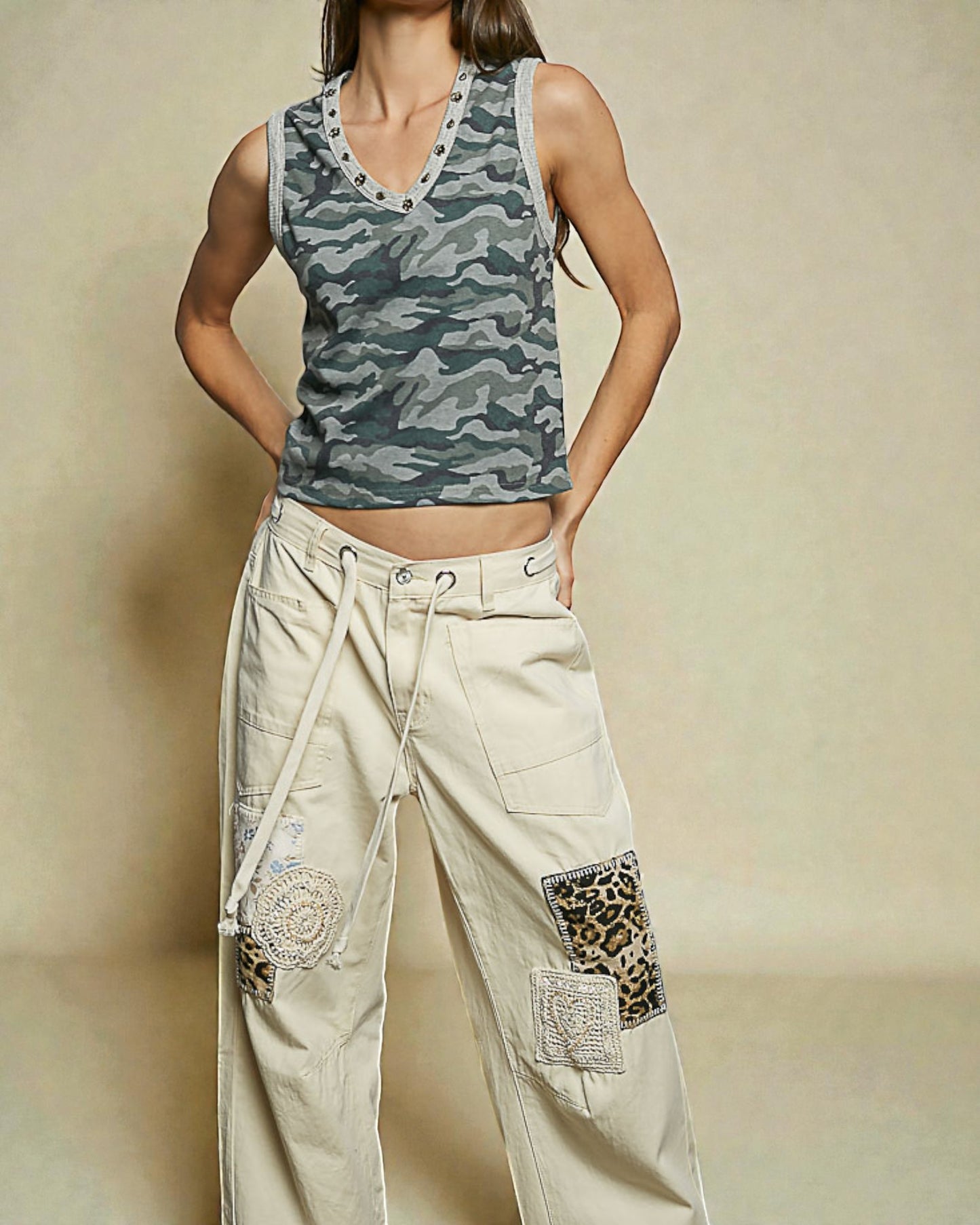 Person wearing a camouflage tank top and beige pants with patches on a beige background