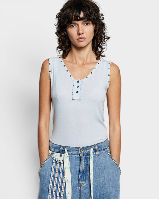 Woman wearing a light blue sleeveless top with button details against a plain background