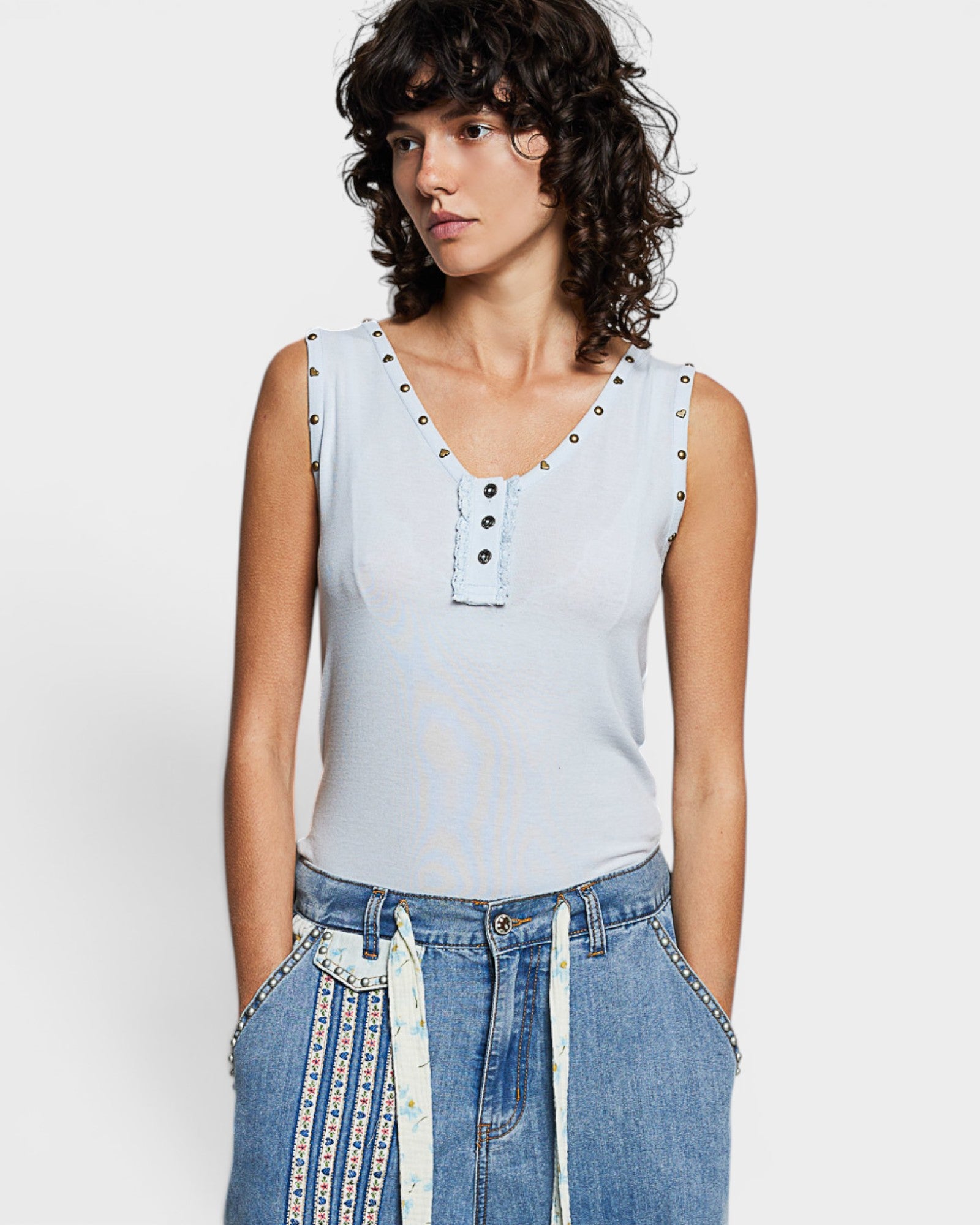 Woman wearing a light blue sleeveless top with decorative buttons on a white background